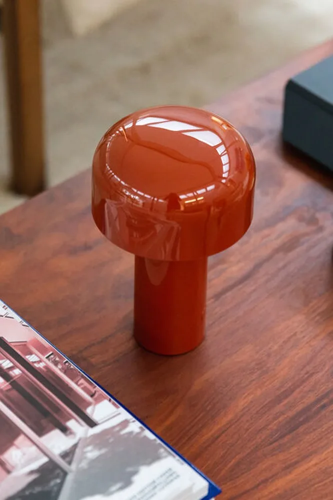 Glossy orange mushroom lamp on a wooden table, with a magazine in the foreground.