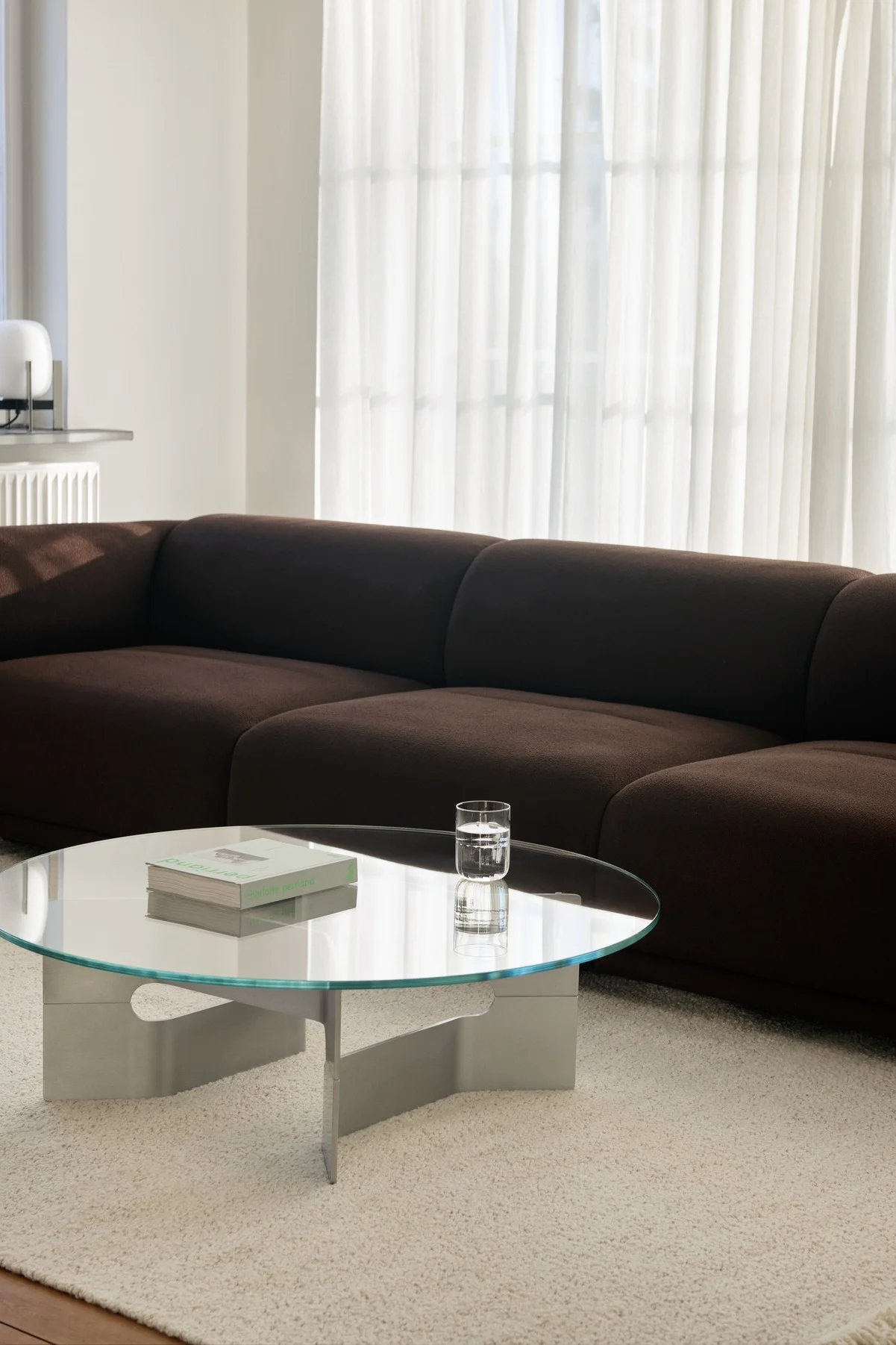 Modern living room with a dark brown modular sofa, round glass coffee table, and light shaggy rug.
