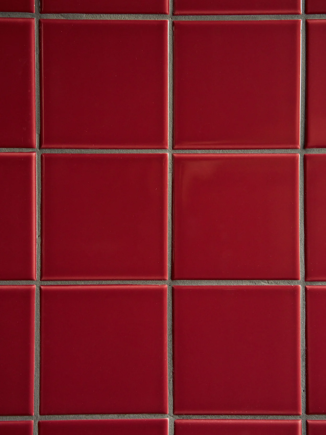 A grid of glossy, square red tiles with dark grey grout.