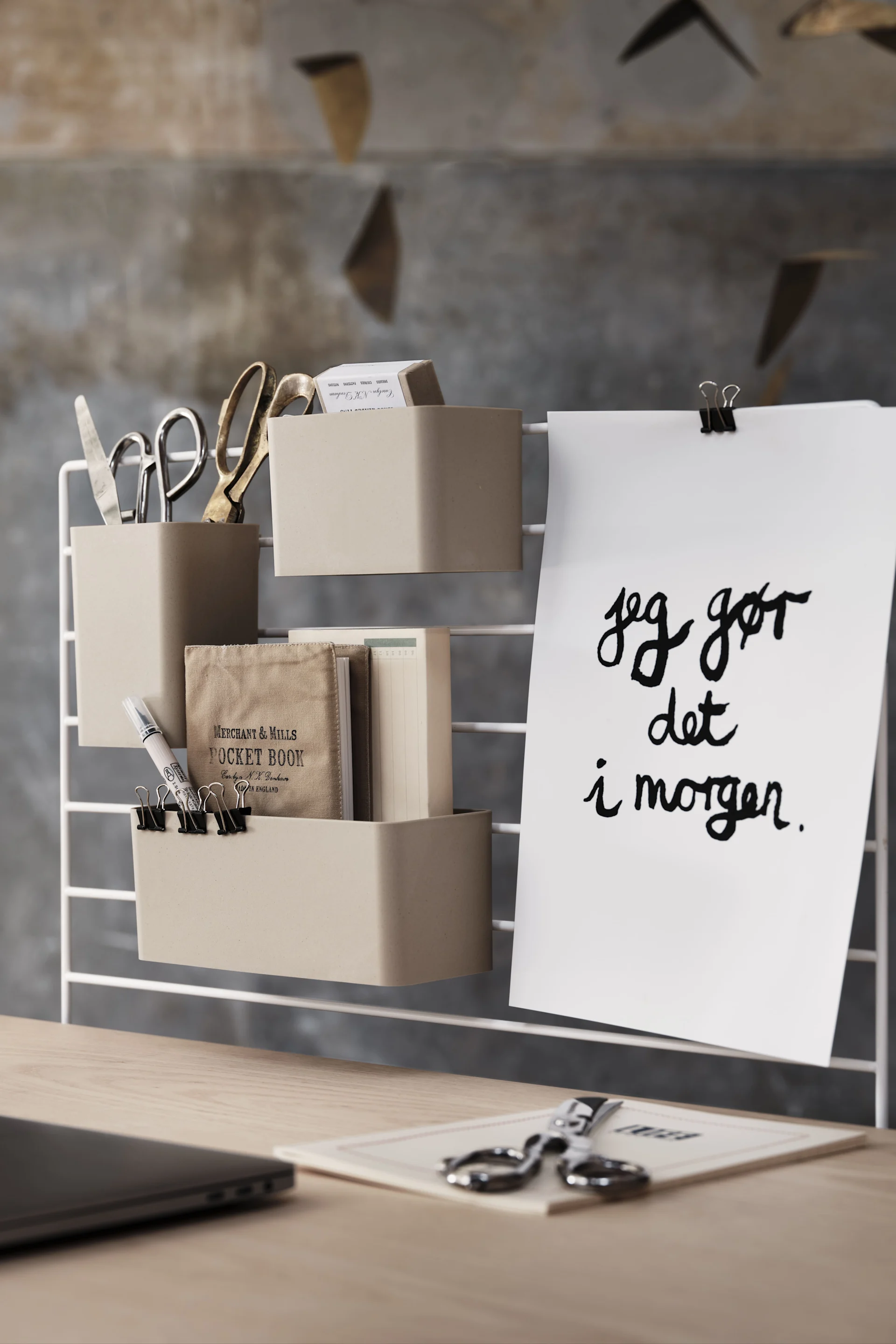 Desk organizer with beige containers holding scissors, notebooks, and clips. A note reads "Jeg gør det i morgen".