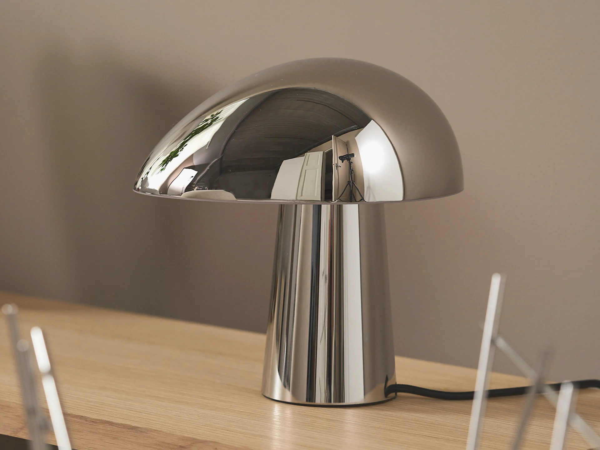 A chrome mushroom-shaped table lamp with a reflective domed shade and cylindrical base, sitting on a light wood surface.
