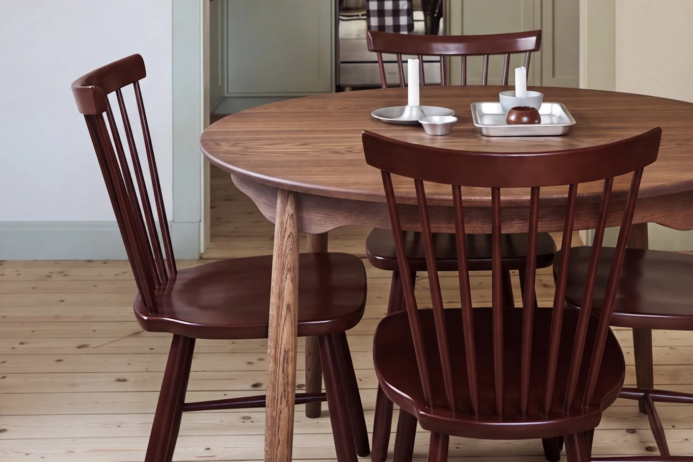 Dining room with a round wooden table, red chairs, and a red pendant light, looking into a kitchen with light green cabinets.