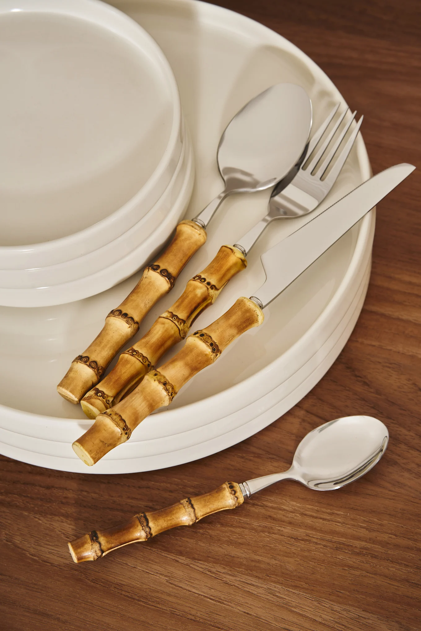 Cutlery with bamboo handles on a stack of white ceramic plates and a wooden table.