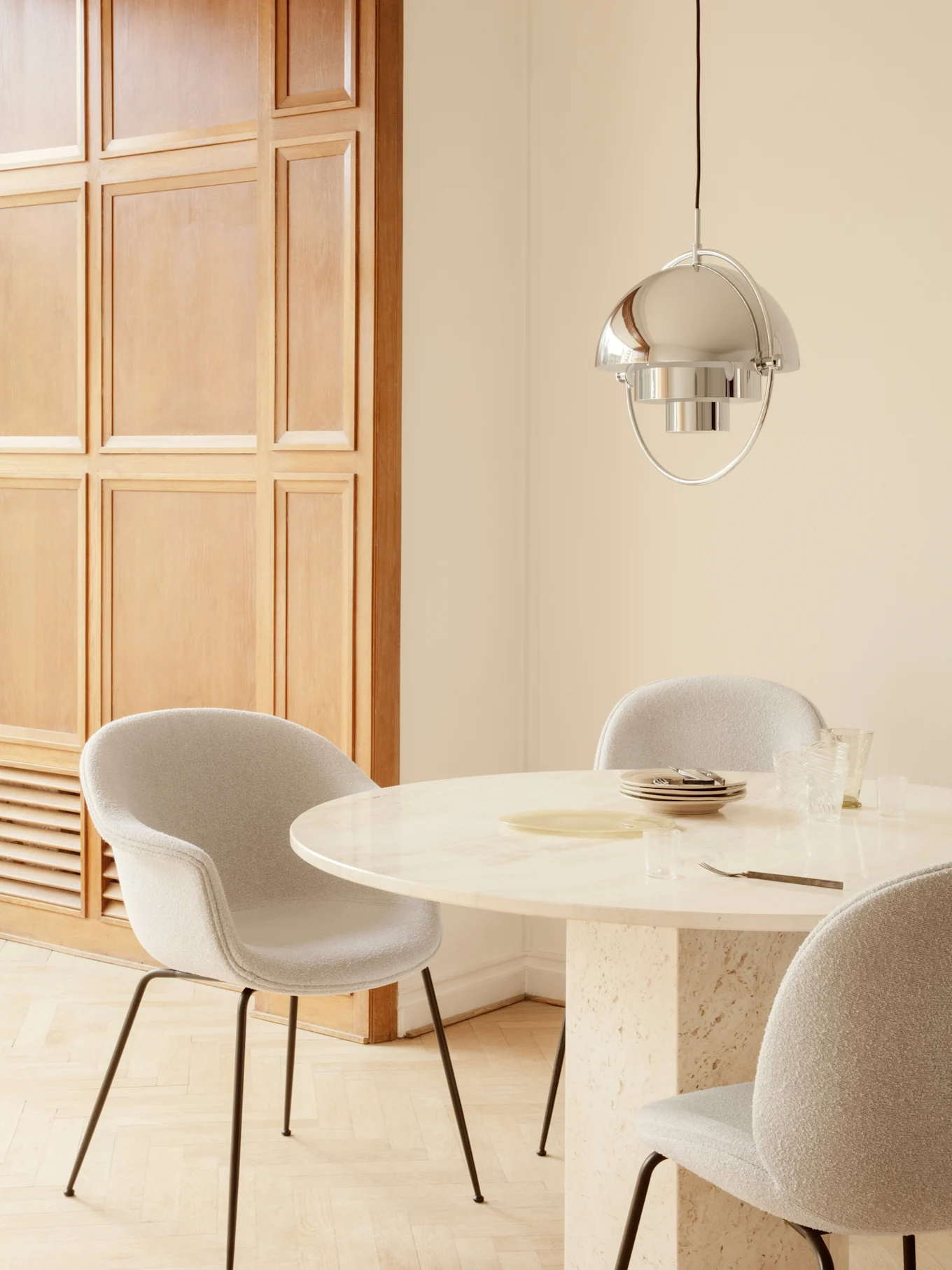 Dining room with round marble table, light gray upholstered chairs, and a polished silver pendant lamp.