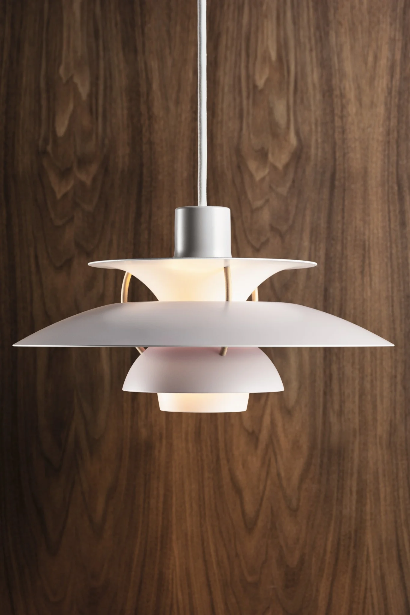 White multi-layered pendant lamp illuminated, hanging against a dark wood grain background.