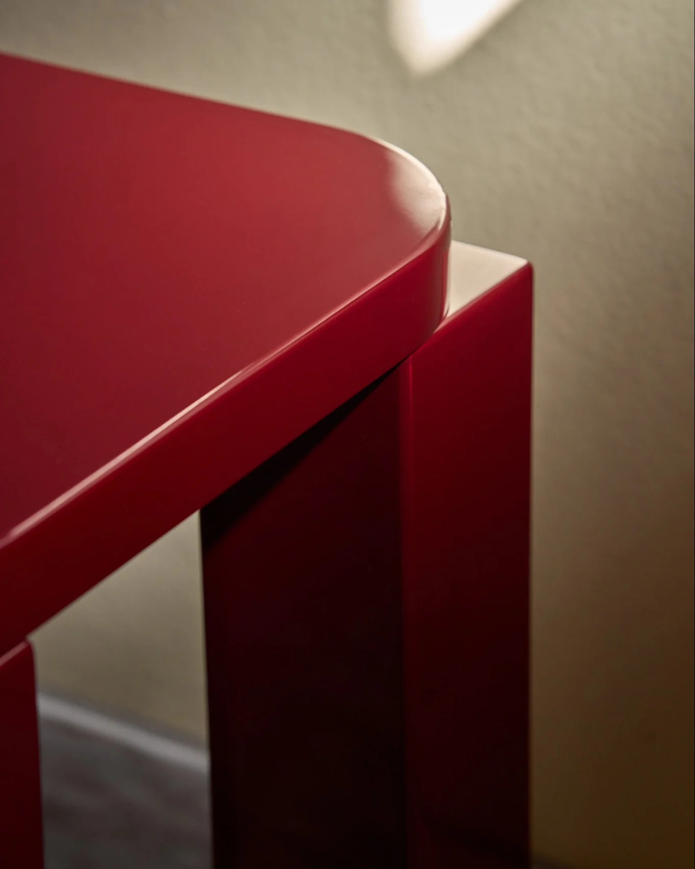 A glossy red stool with a rounded rectangular top, on a tiled floor next to a wall with red tiles.