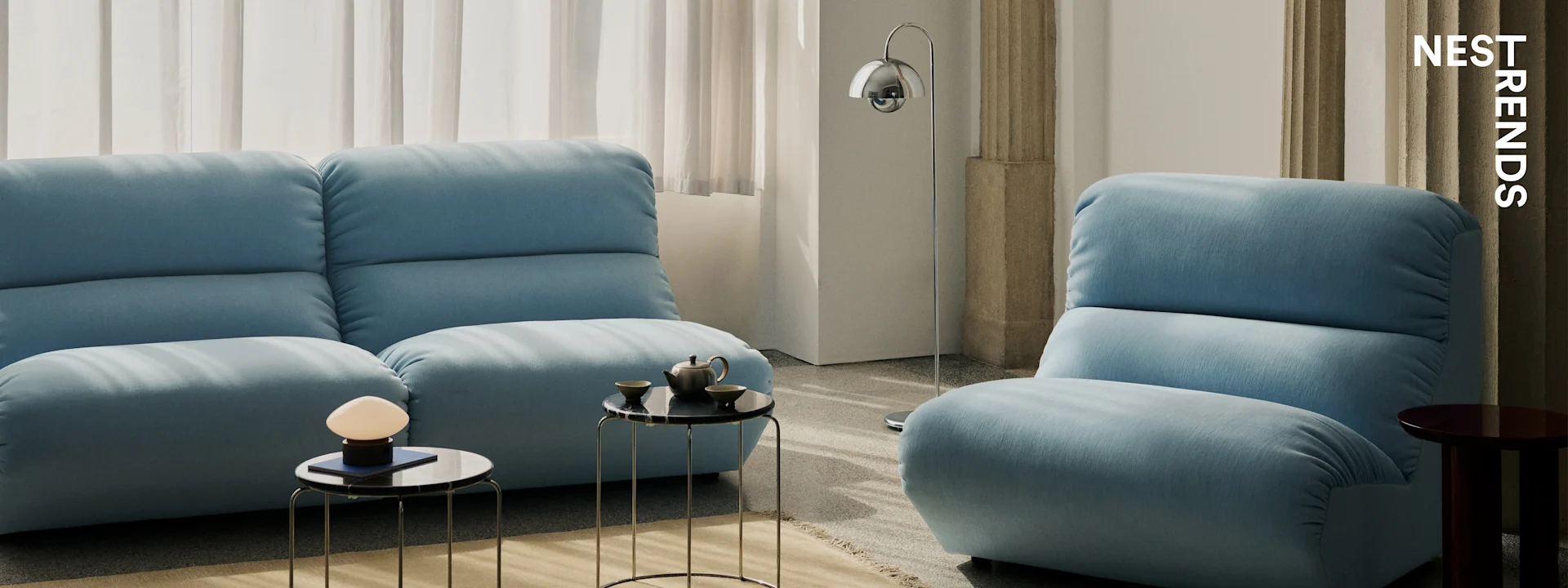 Modern living room with two light blue sofas, black marble-top side tables, and sleek lamps.