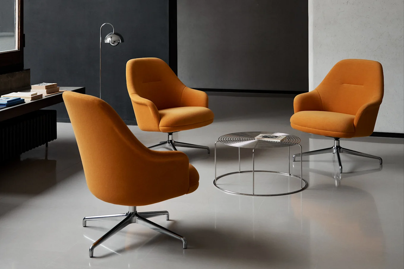 Three orange swivel armchairs gathered around a round chrome coffee table in a modern room.
