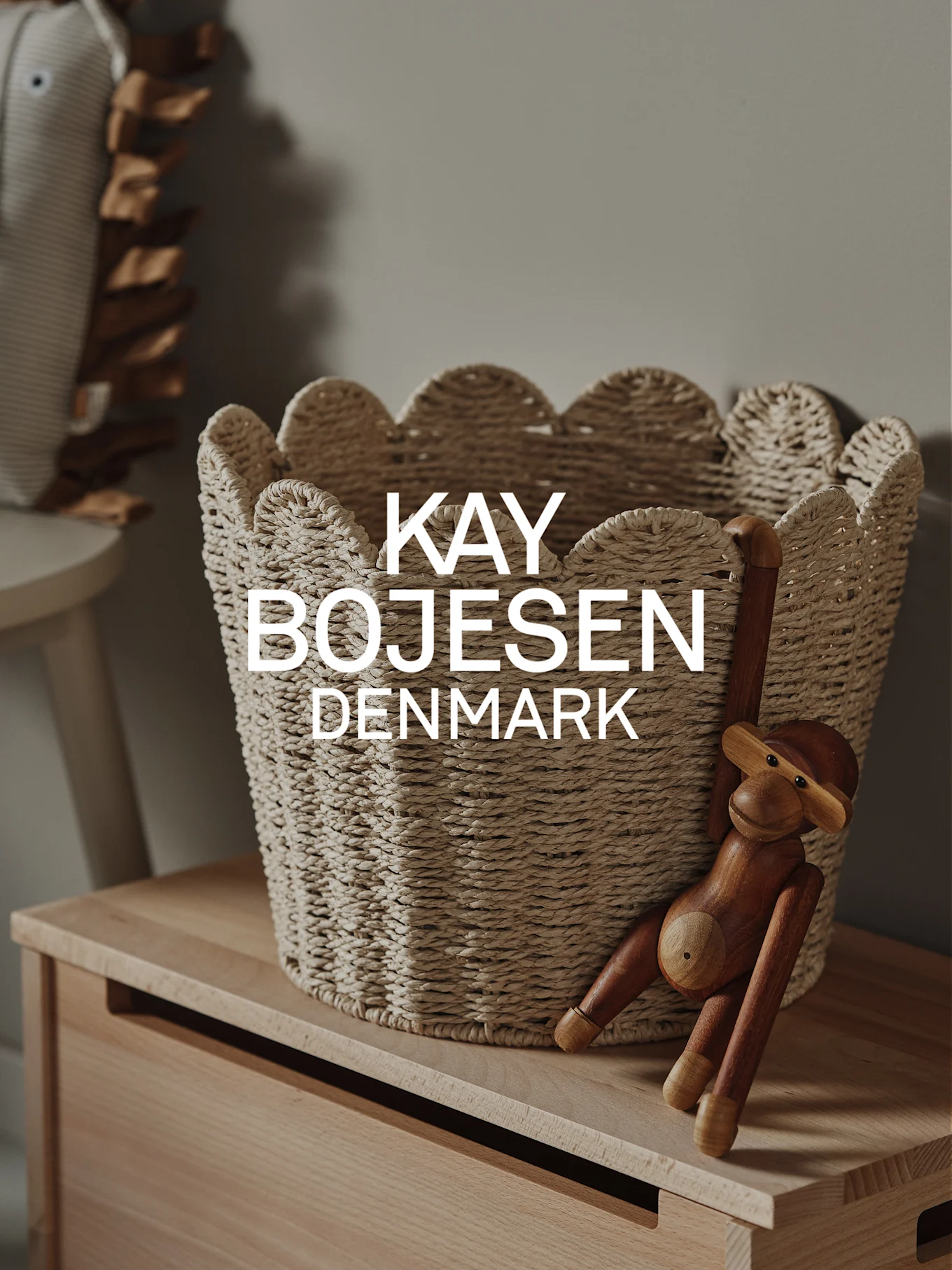 A natural woven basket with scalloped edges and a wooden monkey toy hanging on a light wood cabinet.
