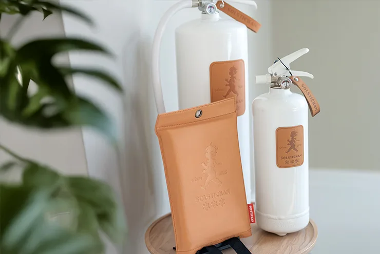 Two white fire extinguishers with tan leather labels featuring the Solstickan logo, next to a matching tan leather pouch.