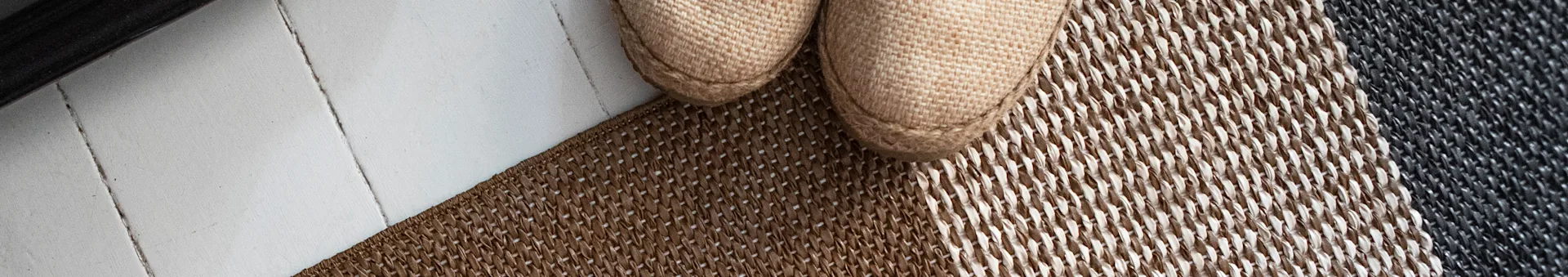 Pair of light brown woven espadrille shoes on a striped brown and grey rug.