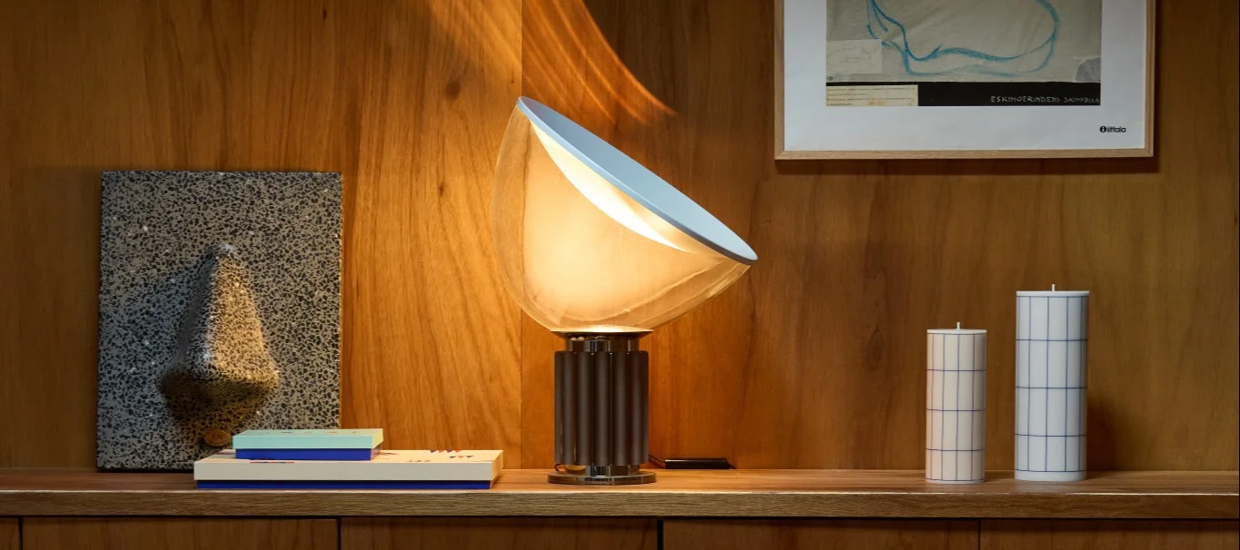 Wooden shelf with silver fluted vase holding dark hydrangeas, a burgundy dome lamp on books, and a silver candlestick with orange candles.