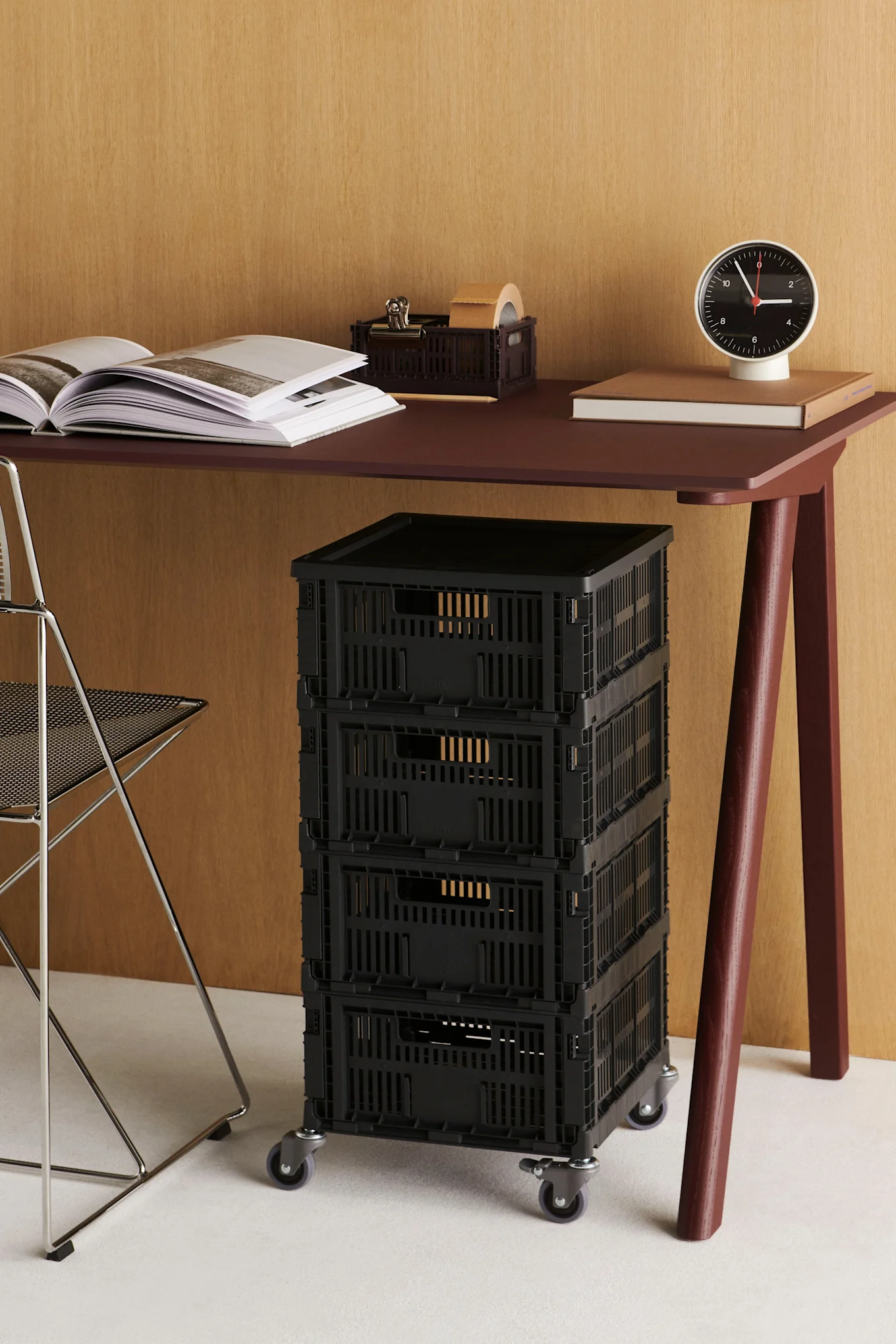 Burgundy desk with open book, clock, and brown organizer. Four black storage crates on wheels beneath.