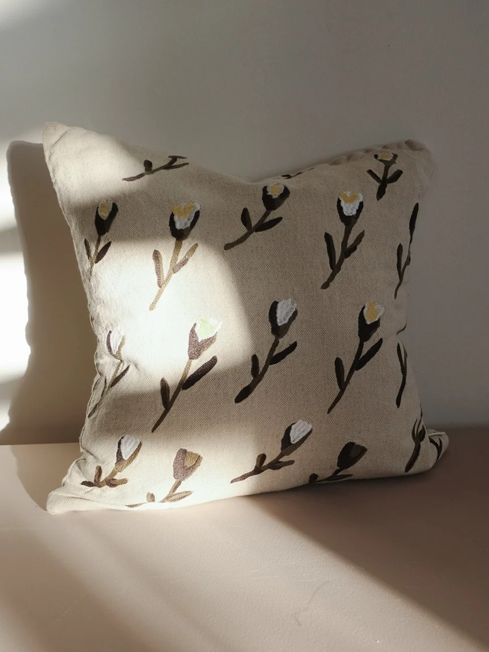 Light beige cushion with a pattern of stylized dark brown and white flowers.