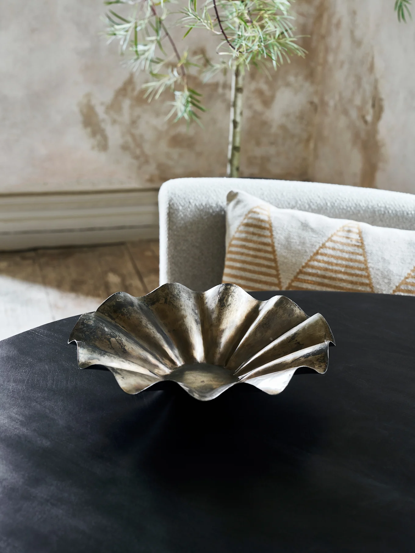 A decorative metallic bowl with a wavy, ruffled edge sits on a dark table in a living room.