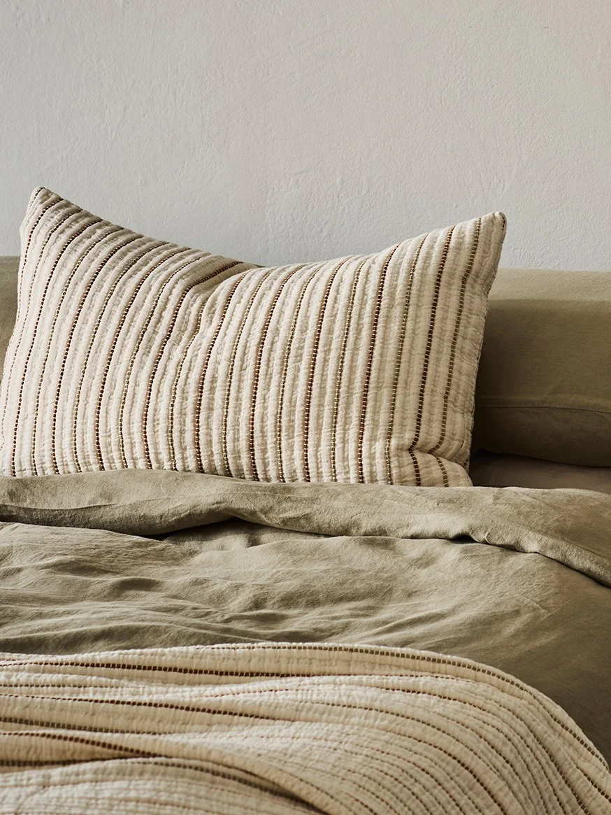 A striped pillow on an olive green bed with a matching striped blanket.