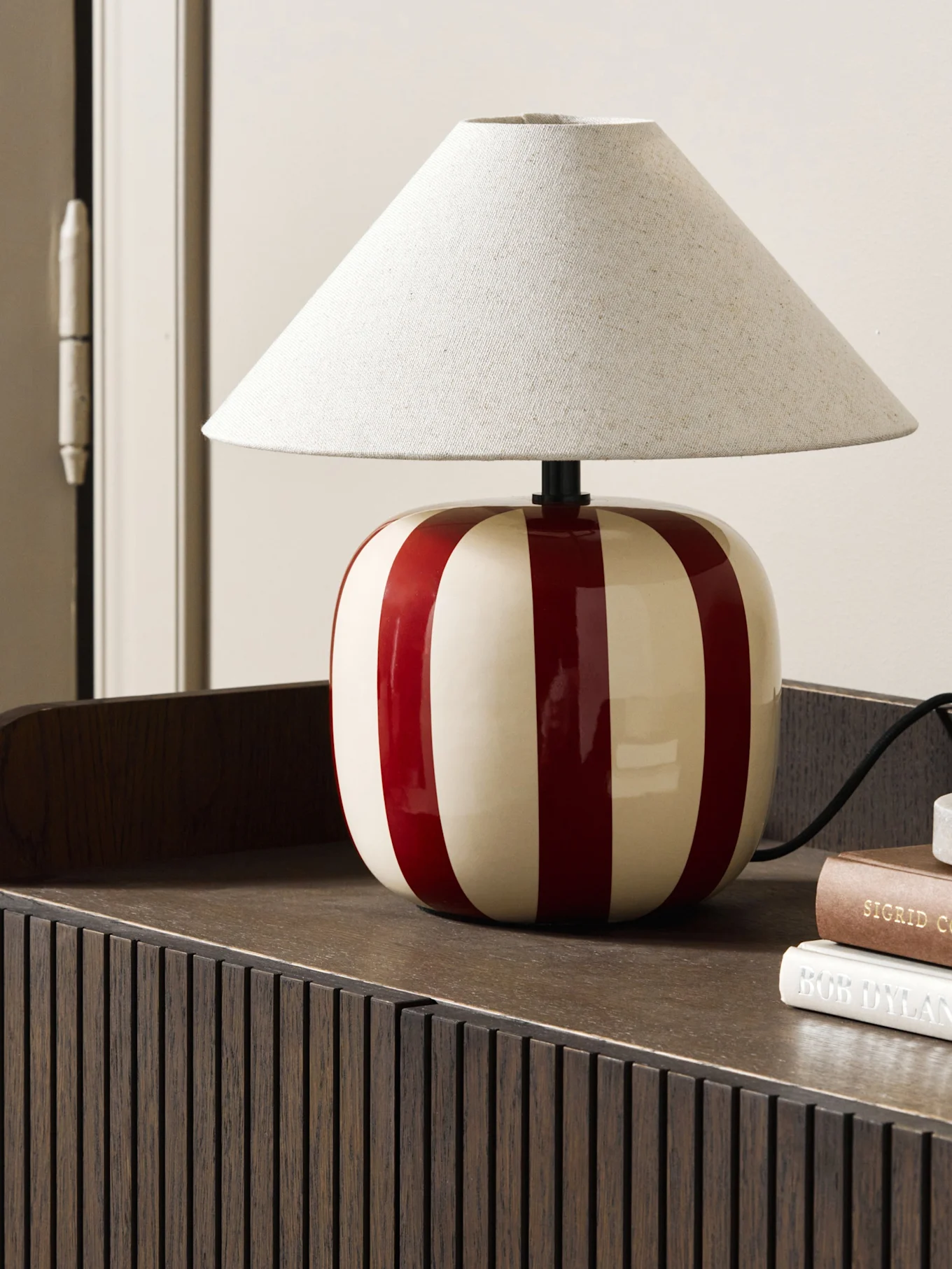 Light blue mushroom-shaped table lamp on a reddish-brown book, on a scalloped shelf.