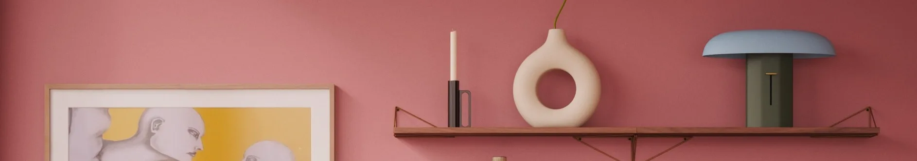 Pink wall, wooden shelf: white candle, cream donut vase with green stem, blue/green lamp. Framed artwork left.