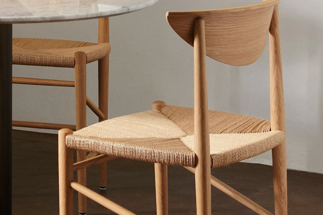 Close-up of two light wood chairs with woven seats, one under a marble table.
