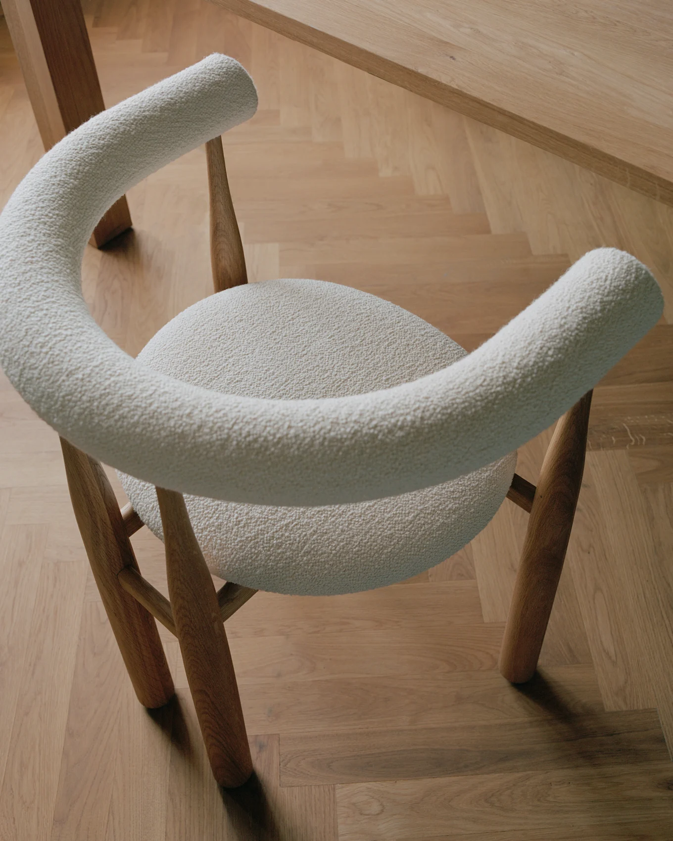A modern chair with light cream boucle upholstery and wooden legs, on a light wooden parquet floor.