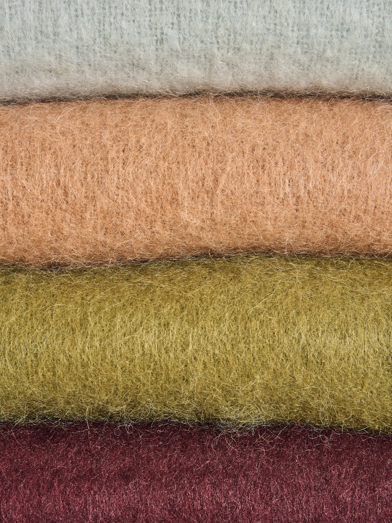 Four rolls of fuzzy fabric in light grey, light brown, olive green, and dark red, stacked horizontally.
