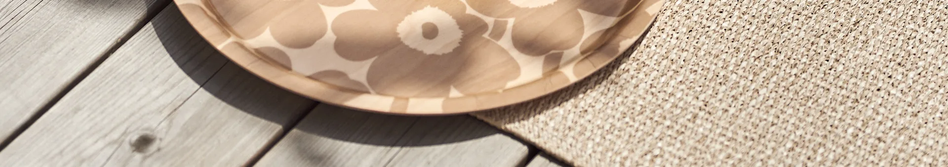 Close-up of a round, light brown tray with a floral pattern, partially on wooden planks and a woven rug.