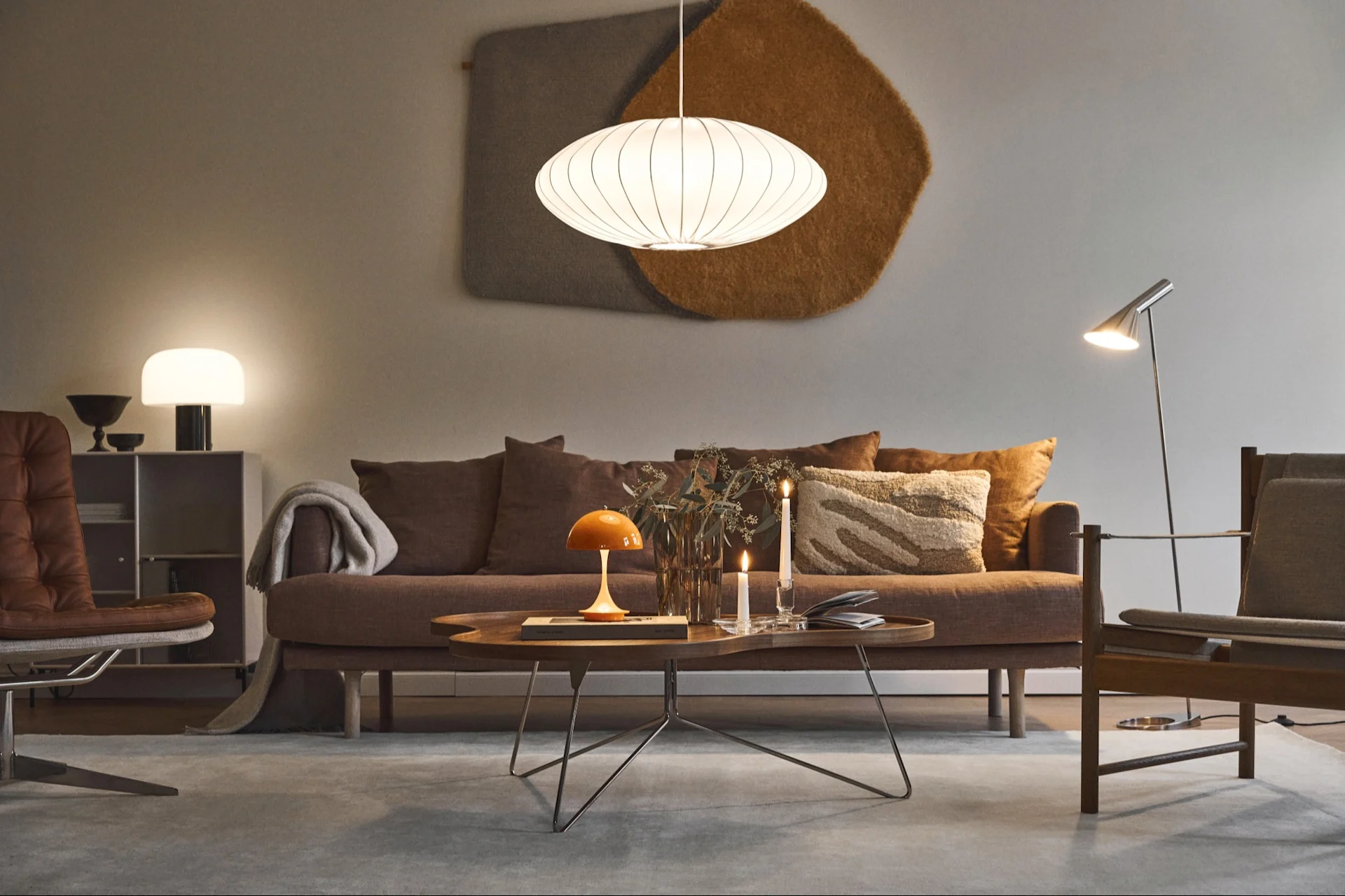 A stylish living room featuring a brown sofa, wooden coffee table with an orange lamp, and a distinctive white oval pendant light.