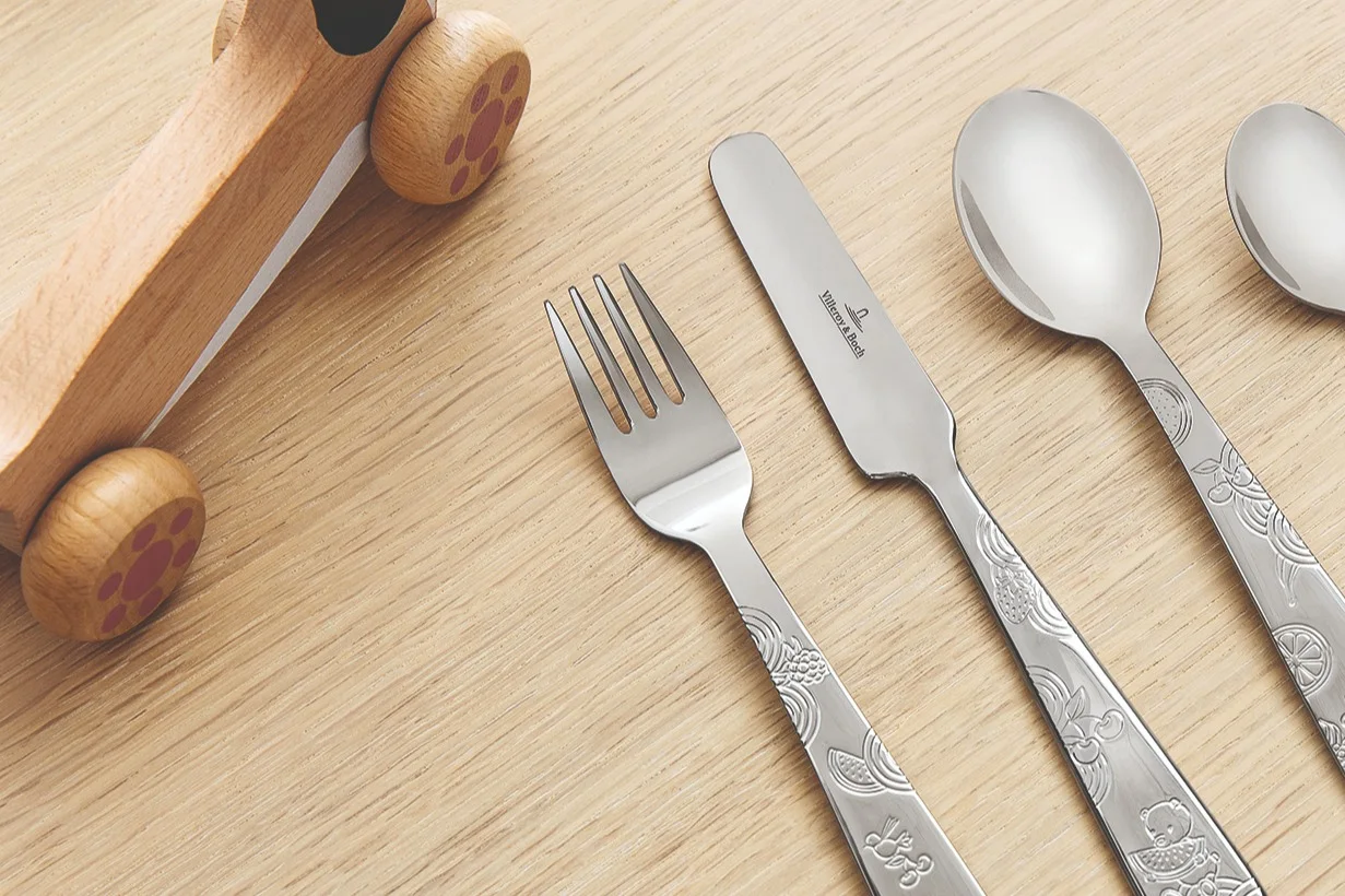 Children's cutlery set with playful bear and fruit engravings by Villeroy & Boch, next to a wooden toy car.