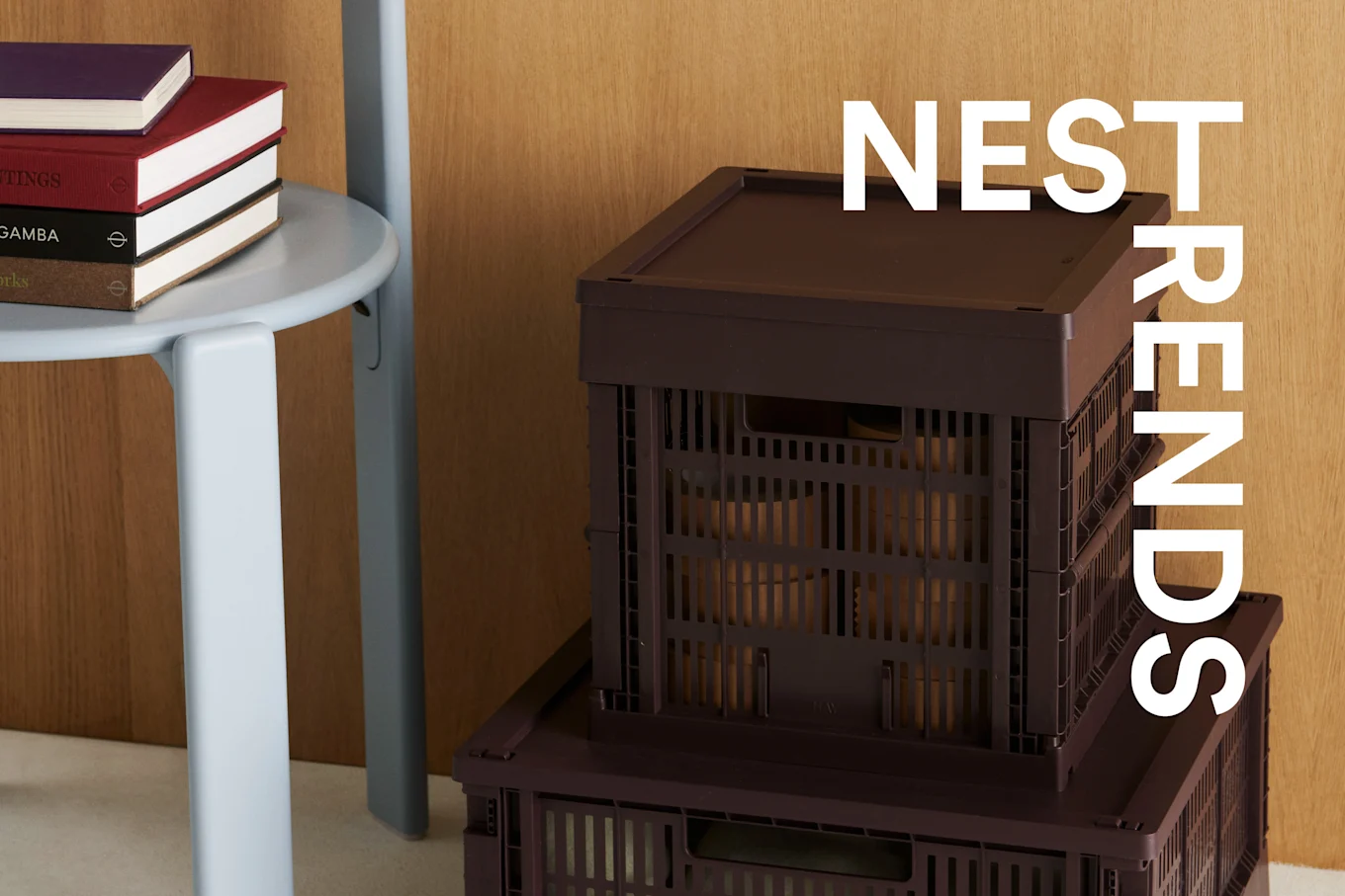 A stack of colorful books on a light grey stool next to two dark brown storage crates, with 'NEST TRENDS' overlaid.