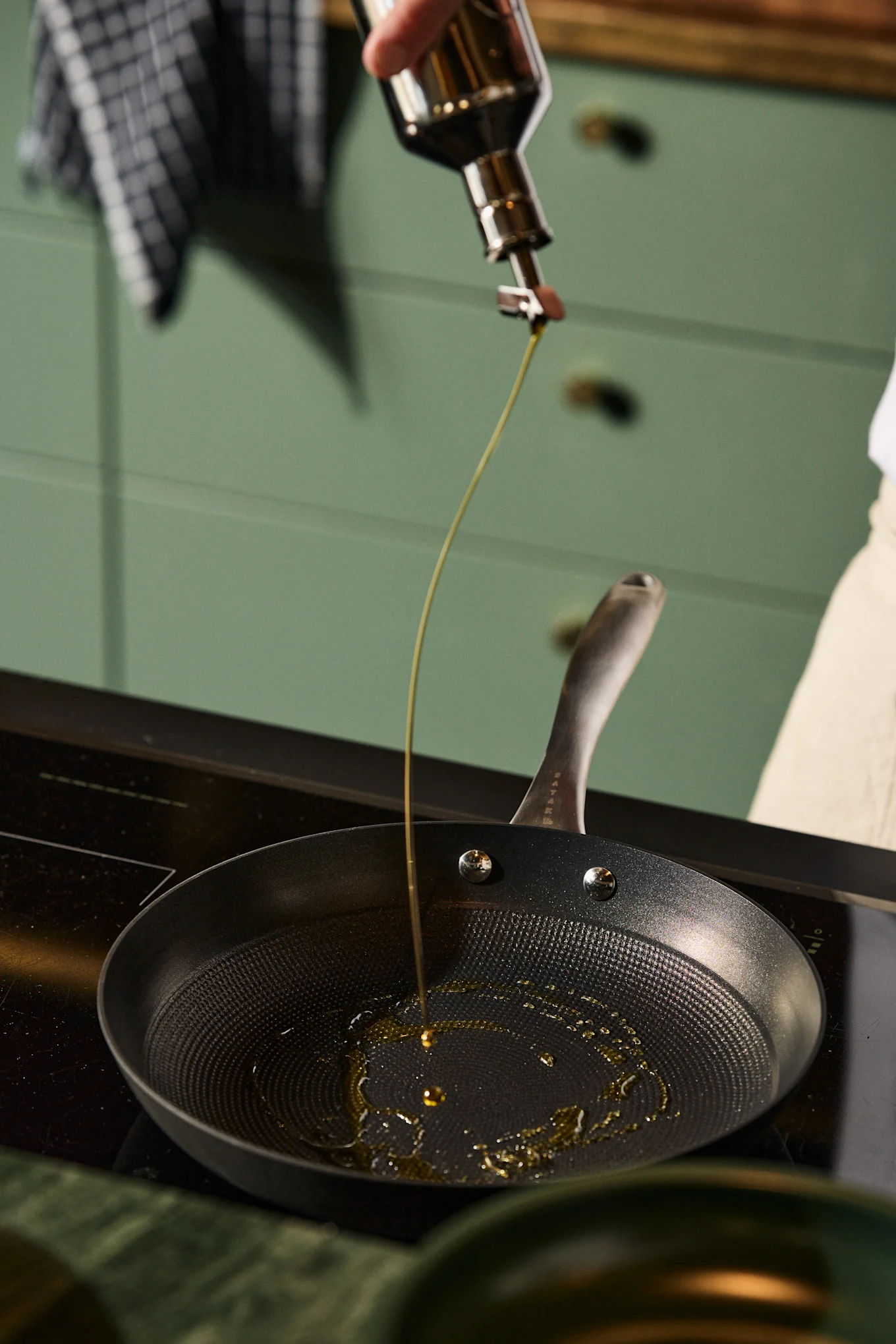 Olive oil being poured into a black frying pan on a stovetop.
