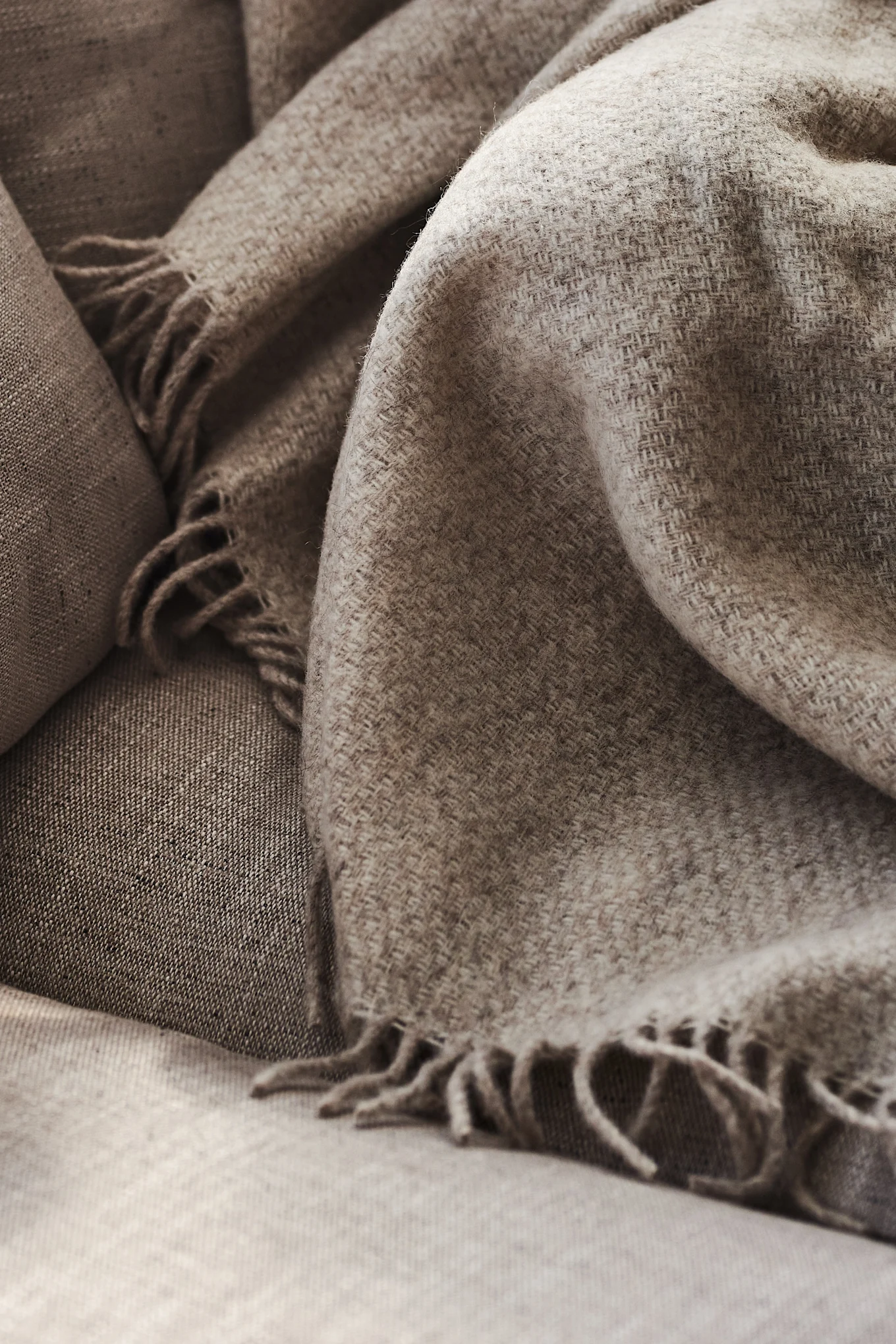 Close-up of a cozy light brown woven blanket with fringes draped over a matching sofa.