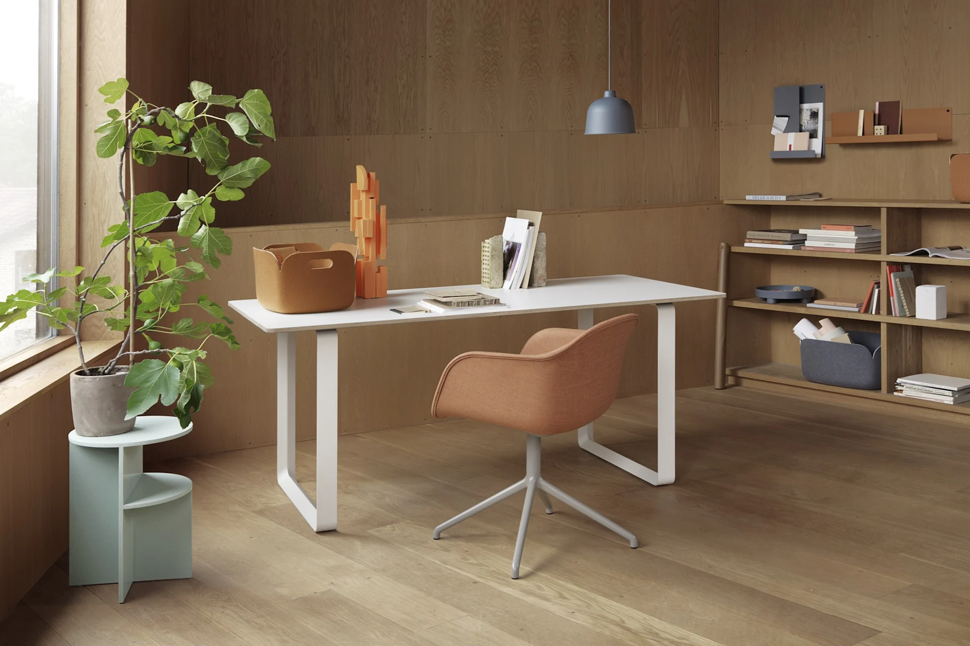 A modern home office with a white desk, an orange chair, and a potted fig tree, against wood-paneled walls and shelves.