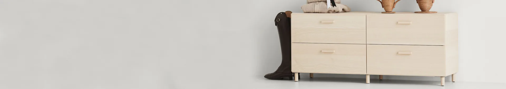 Light wood cabinet with four drawers, a tall brown boot, knitwear, and decorative items on top.
