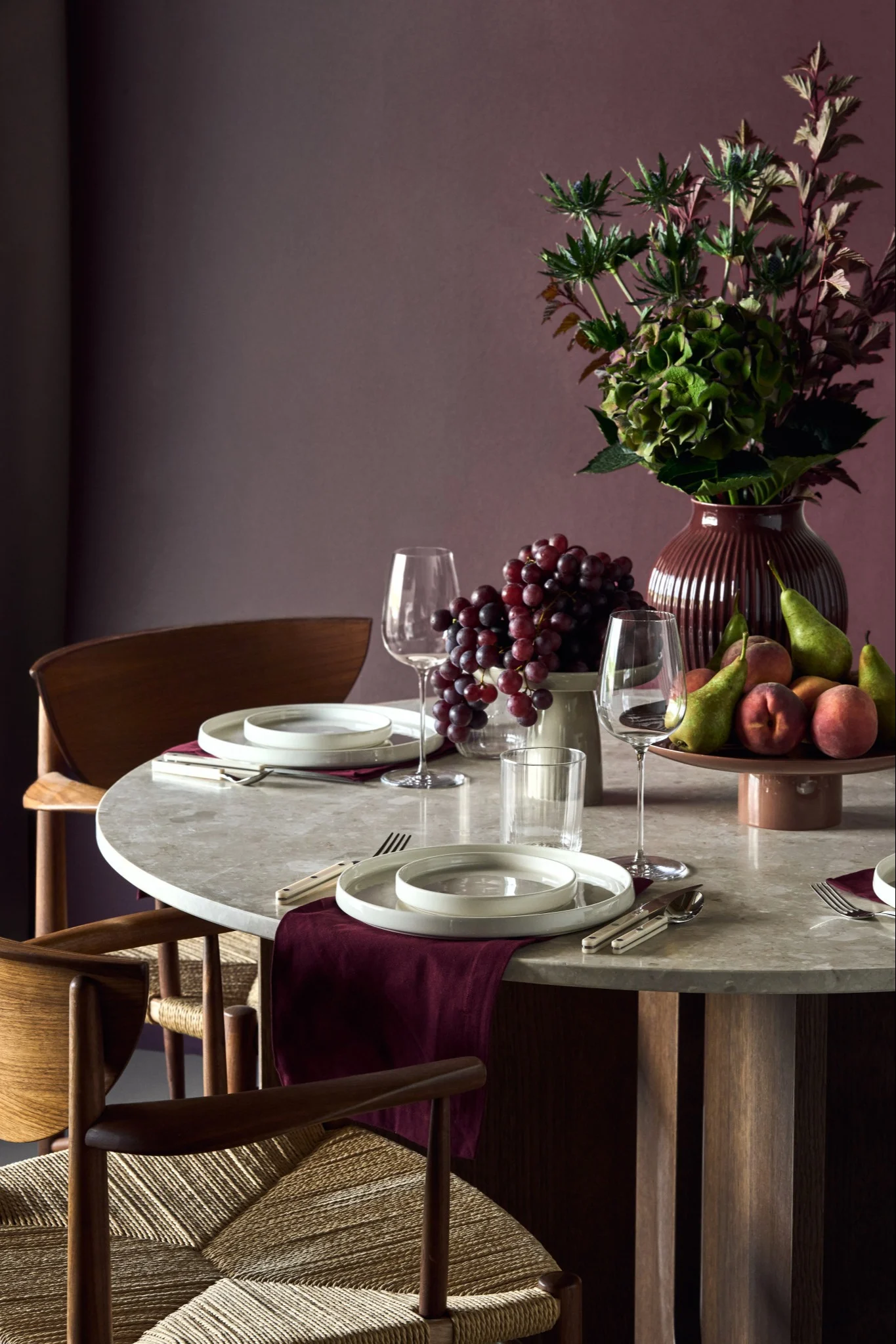 A stone table paired with wooden chairs is set with white porcelain and deep wine-red details that reflect the interior design trends of 2026.