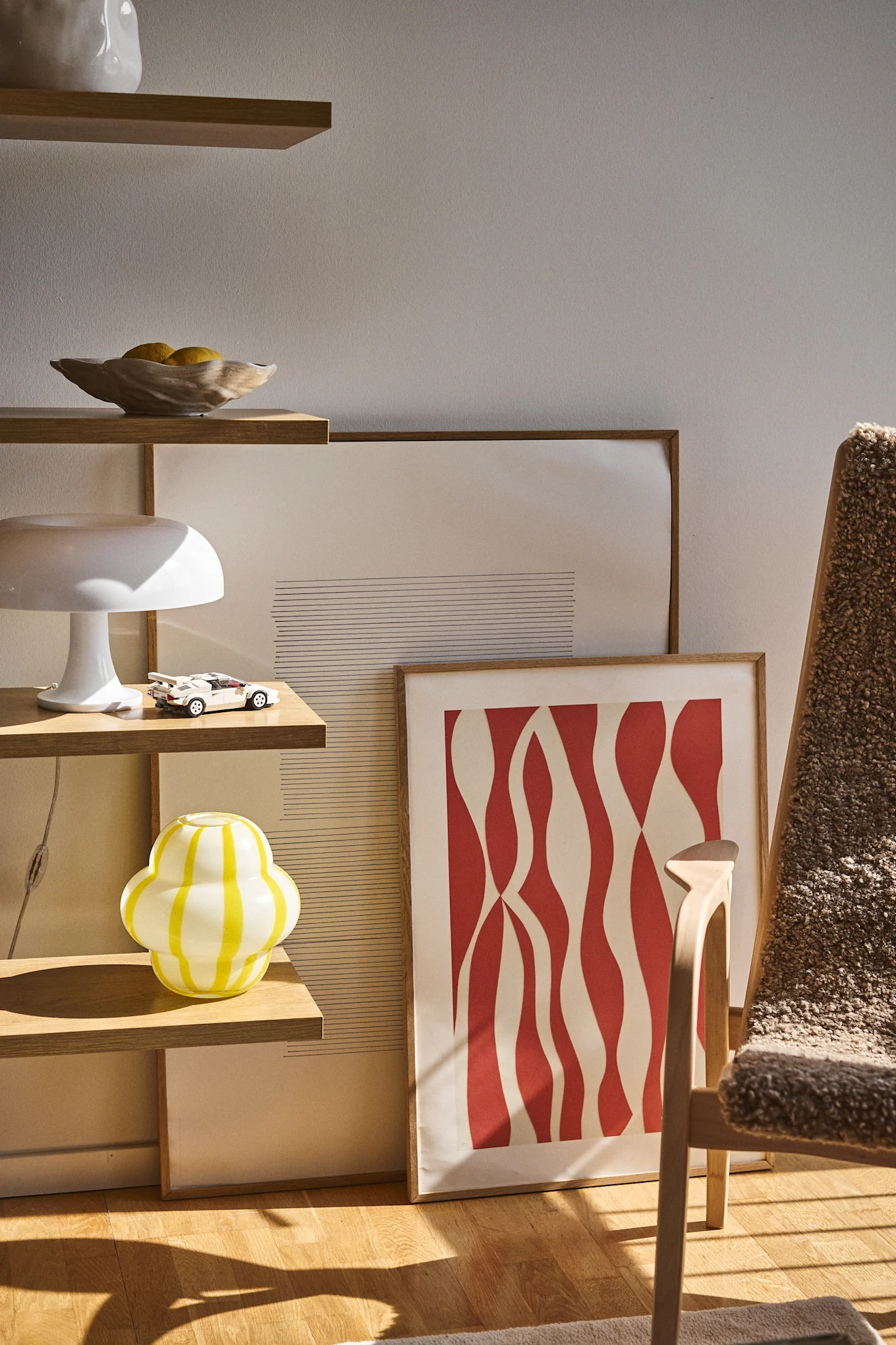 A shelf with a playful yellow vase, placed next to artworks leaning against the floor and an armchair – an unexpected and colorful interior that follows the interior design trends of 2026.