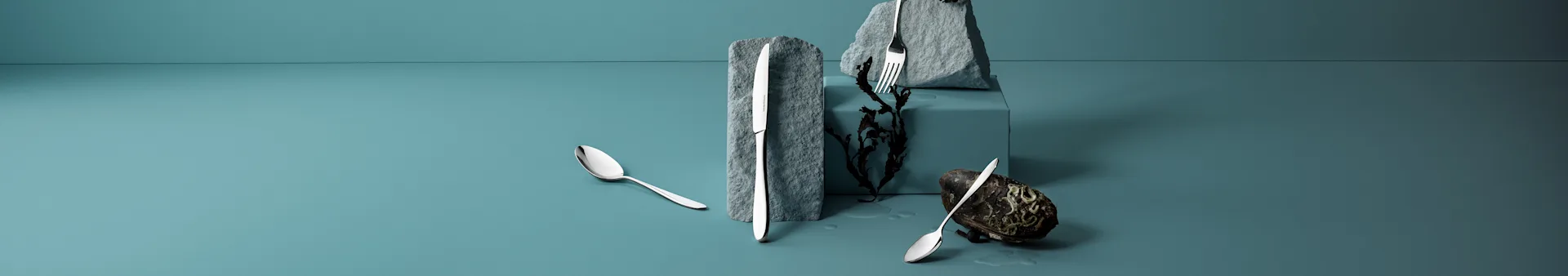 Silver cutlery arranged on a teal surface with rocks, seaweed, and a dark shell.