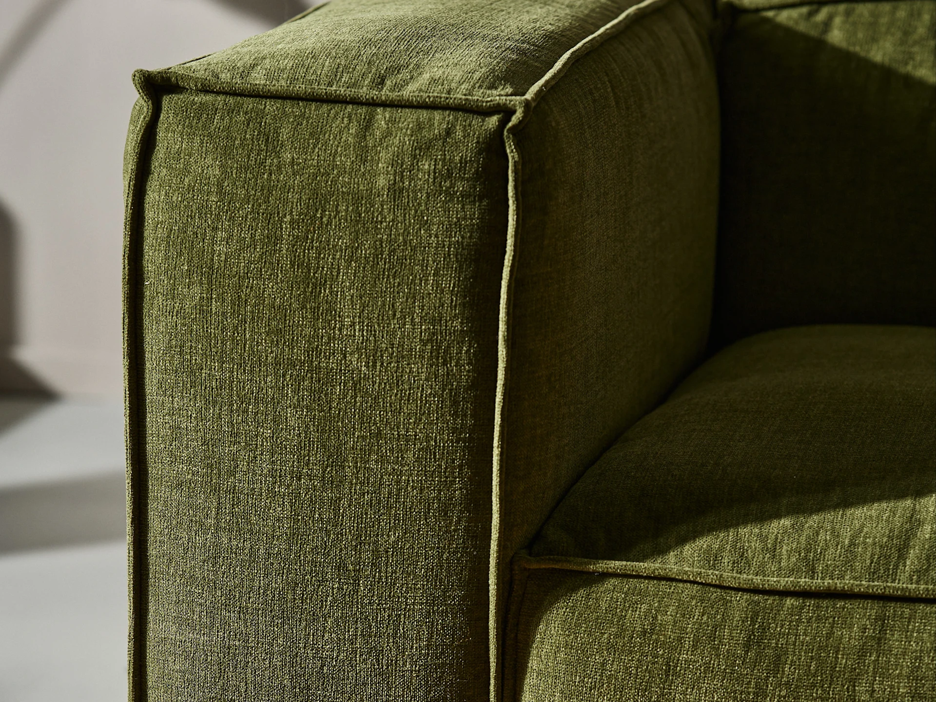 Close-up of a green fabric sofa armrest with visible texture and piping.