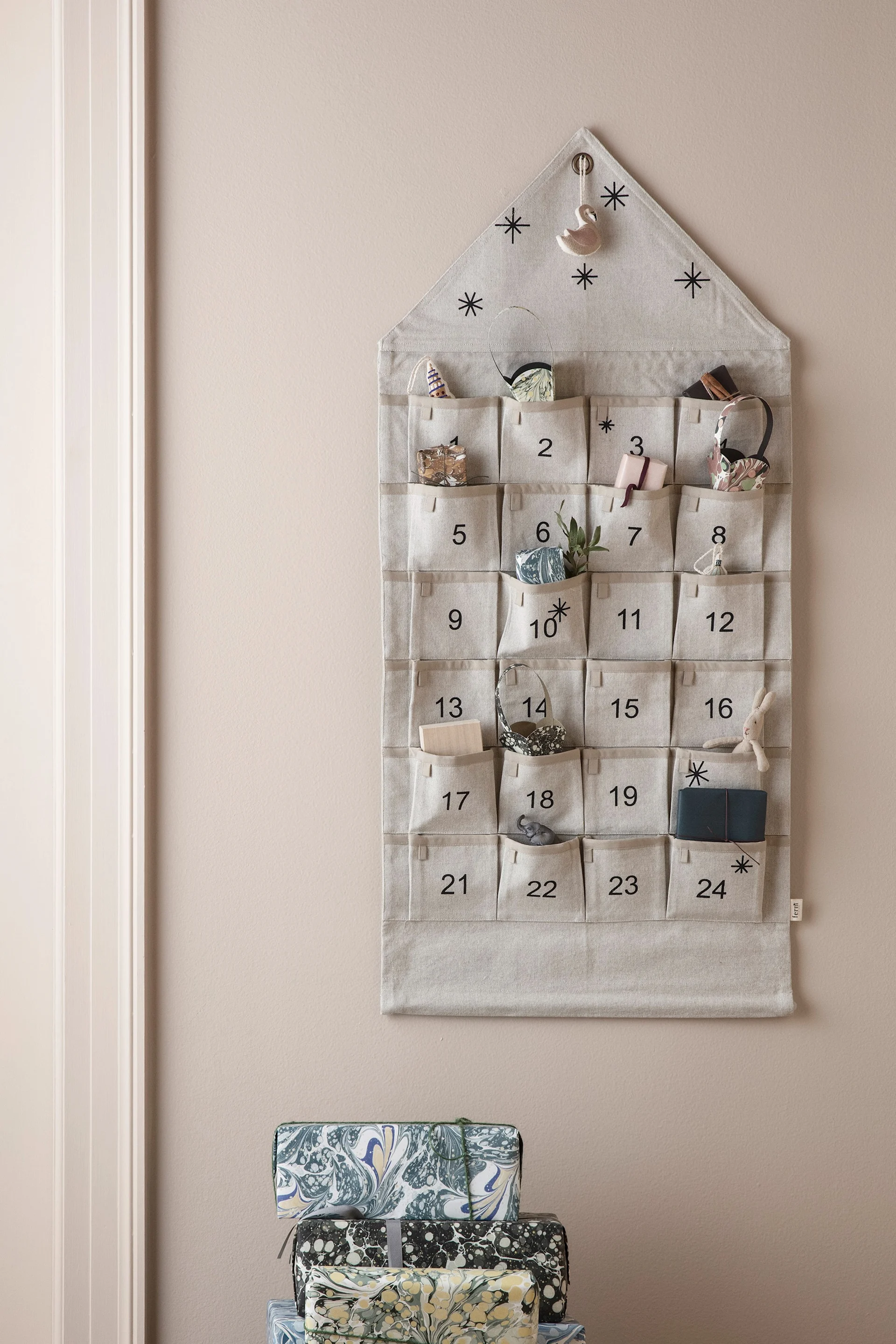 Fabric advent calendar with numbered pockets and small gifts, hung on a wall above stacked marbled-pattern presents.